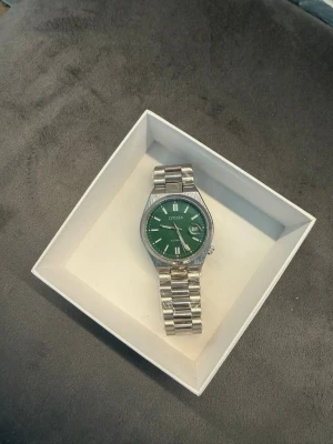 Citizen klocka med grön urtavla - Stilren Citizen klocka med grön urtavla och silverfärgad länk i metall. Klassisk design med datumvisning och tydliga indexmarkeringar. Perfekt accessoar för dig som vill ha något unikt på handleden.