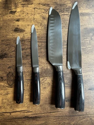 Set med fyra köksknivar i stål - Säljer ett set med fyra köksknivar i rostfritt stål med mörka träliknande handtag. Setet innehåller olika storlekar för olika användningsområden, från mindre skalkniv till större kockkniv. Perfekt för matlagning hemma och snygga att ha framme på köksbänken.