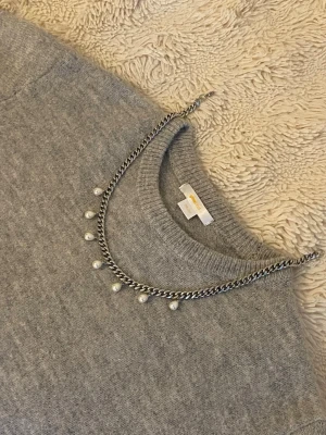 Silverfärgat halsband med pärlor - Snyggt silverfärgat halsband med kedja och hängande pärlor. Passar perfekt till stickade tröjor eller som ett statement-smycke till vardags och fest. Halsbandet syns här tillsammans med två olika stickade tröjor i grått och beige. Köp direkt eller ge prisförslag!