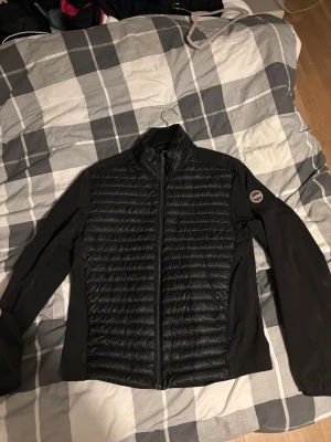 Svart jacka från Colmar - Snygg svart pufferjacka från Colmar med quiltad framsida och släta ärmar. Jackan har hög krage, hel dragkedja och en logotyp på ärmen. Perfekt för varmare dagar och enkel att matcha med olika outfits. Köpt för 2500. Finns inte att köpa någonstans.