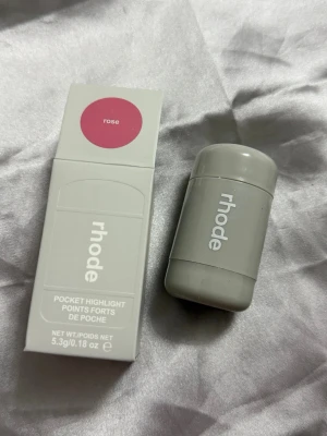 Rhode Pocket Highlight Rose - Säljer en Rhode Pocket Highlight i färgen Rose. Kommer i en smidig grå stick-förpackning och matchande ask. Perfekt att ha med i väskan för glow on-the-go. Innehåller 5,3g. Ger en fräsch, rosig lyster till huden.
