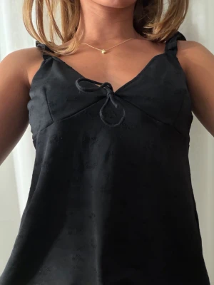 Svart linnetopp med knytband - Snygg svart linnetopp med smala axelband som knyts upptill och en liten knytning framtill vid bysten. Toppen har en v-ringad hals. Perfekt till sommaren och enkel att styla med olika outfits. Samt öppen i ryggen så så så fin. Stoleken är M men liten så funkar som S. Passar bra på mig som alltid har S.