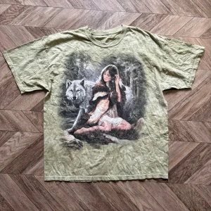 Grön t-shirt med vargmotiv - Cool grön t-shirt med stort tryck av en kvinna och en varg på framsidan. T-shirten har korta ärmar och en relaxed passform. Perfekt för dig som gillar naturinspirerade motiv och vill sticka ut lite extra.