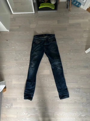Mörkblå Replay jeans med slitningar - Säljer ett par mörkblå jeans från Replay med snygga slitningar och tvättade detaljer. Klassisk femficksmodell med smal passform och normal midja. Perfekta för dig som gillar en avslappnad men ändå trendig stil.