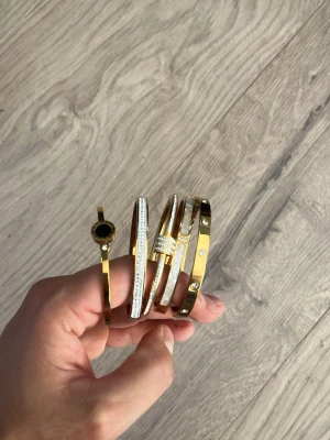 Guldiga armband med stenar och detaljer - 5 stilrena armband i guldfärg, varav ett har svart cirkeldetalj, ett är täckt av gnistrande stenar, och två har infällda stenar och skruvliknande detaljer. Perfekta för att ge din outfit en lyxig touch. 18K äkta i äkta guld plätering. Riktigt bra kvalitet för den som vill lyfta sin outfit. Alla för 199. Svarar inte på skambud 