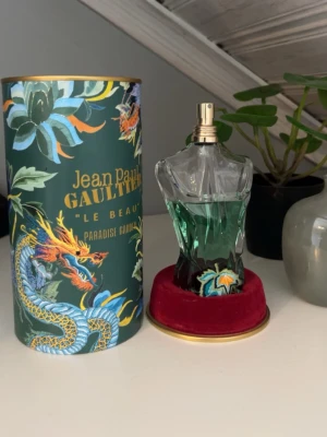 Jean Paul Gaultier Le Beau Paradise Garden - Unik parfymflaska formad som en manlig torso med grön vätska och guldfärgad spray. Kommer i en dekorativ grön tub med drakmotiv och tropiska växter. Lyxig röd sammetsbas. Perfekt för dig som gillar snygg design och starka dofter. Perfekt för everyday use! Lite mer än hälften kvar motsvarar runt 80 ml. Det är en Eua De Parfum. Hör av dig vid frågor! 