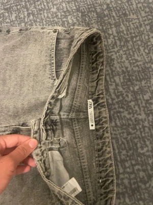 Grå tvättade raka jeans från Zara - Säljer ett par grå tvättade jeans från Zara med rak passform och hög midja. Jeansen har klassisk femficksdesign och är tillverkade i denim. Perfekta för en avslappnad och trendig look.