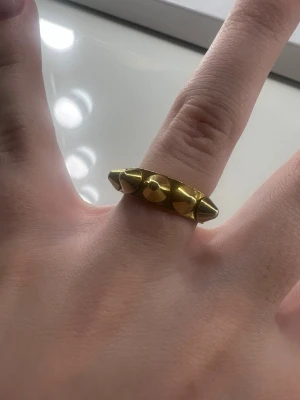 Edblad guldig ring med nitar - Edblad ring i guldfärgad metall med spetsiga nitar runt hela bandet. 