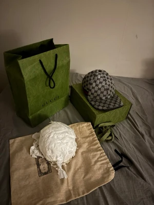 Gucci keps  - Säljer en snygg Gucci keps i beige och brunt med det klassiska GG-monogrammönstret. Kepsen har böjd skärm och justerbar rem bak. Kommer med originalpåse, box och shoppingpåse. Perfekt för dig som vill ha en exklusiv och trendig accessoar.