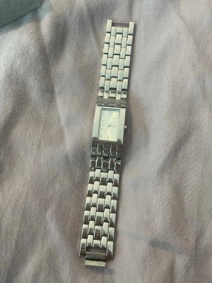 Rektangulär silverfärgad klocka - Stilren klocka i silverfärg med rektangulärt ur och länkarmband i metall. Urtavlan är ljus med minimalistiska markeringar och diskret design. Perfekt accessoar för dig som gillar en clean och modern look.
