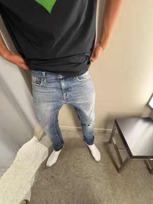 Tiger of Sweden  - Säljer ett par ljusblå jeans med klassisk femficksdesign och dragkedjegylf. Jeansen har en lätt tvättad look och sitter gött över benen. Perfekta för en avslappnad och trendig stil.