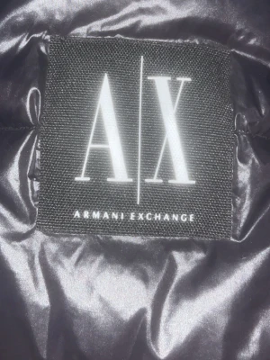 Svart pufferjacka från Armani Exchange -  Pris kan diskuteras. Säljer en svart pufferjacka från Armani Exchange i storlek M. Jackan har en glansig finish, dragkedja framtill och två sidofickor med dragkedja. Perfekt för kalla dagar. Ny pris 3000kr.