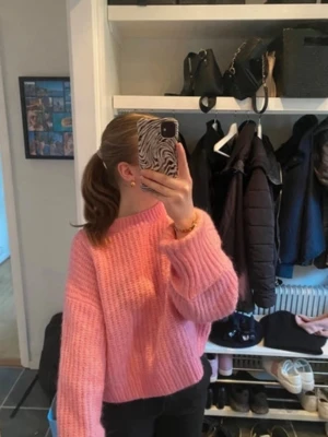 Rosa oversized stickad tröja - Säljer en oversized stickad tröja i en härlig rosa färg. Tröjan har breda ribbstickade ärmar och en hög, rund halsringning. Perfekt för dig som gillar en avslappnad och trendig look. Modellen på tröjan är lite kort.