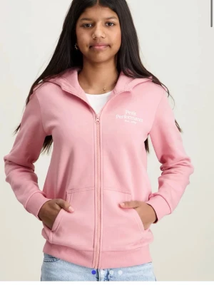 Rosa hoodie Peak Performance - Säljer en ljusrosa hoodie från Peak Performance med dragkedja framtill och två fickor. Tröjan har ribbade muddar vid ärmslut och nederkant samt logga på bröstet. Perfekt för en avslappnad och sportig stil.