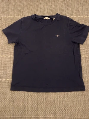 GANT T-Shirt - En enkel mörkblå t-shirt i bomull med rund hals och korta ärmar. Liten diskret logga på bröstet. Perfekt till jeans eller shorts för en clean och stilren look.