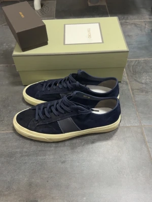 Tomdord sneakers  - Snygga mörkblå sneakers i mocka med vit sula och mörkblå snörning. Skorna har en klassisk låg profil och en diskret grå detalj på sidan. Perfekta för en stilren och avslappnad look.