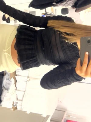 Svart långärmad volangblus - Säljer en svart långärmad blus med transparenta partier och volang nedtill. Toppen har en figurnära passform och fina detaljer i spets och ribbad struktur. Toppen är lite genomskinlig och perfekt en dag då du ska klä upp dig lite mer💕🤗