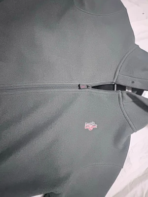 Mörkgrön hoodie från Moncler - Snygg mörkgrön hoodie från Moncler med dragkedja framtill och broderad logga på bröstet. Tillverkad i ett mjukt och bekvämt material, perfekt för en avslappnad stil. Klassisk huva och minimalistisk design gör den enkel att matcha.