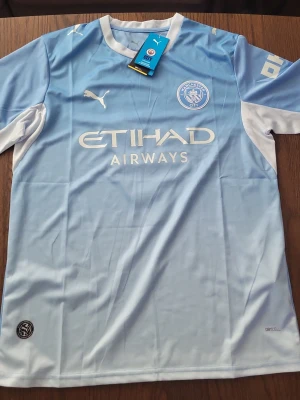 Manchester City ljusblå matchtröja Puma - Säljer en officiell Manchester City matchtröja från Puma i ljusblått med vita detaljer. Tröjan har klubbmärke och Puma-logga på bröstet samt Etihad Airways-tryck framtill. Tillverkad i syntetmaterial och perfekt för fotbollsträning eller match.