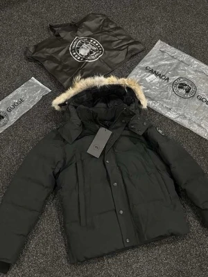 Svart dunjacka med pälskant - Säljer en svart dunjacka från Canada Goose med avtagbar huva och snygg pälskant. Jackan har flera fickor, tryckknappar och dragkedja framtill. Klassisk patch på ärmen och varm vaddering som passar perfekt för kalla vinterdagar.