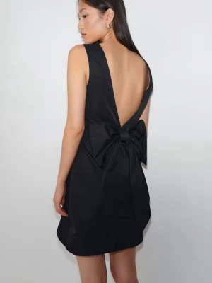 Elegant cocktailklänning med rosett - Stilren svart kort klänning med öppen rygg och stor dekorativ rosett baktill. Klänningen är ärmlös och har en enkel, elegant siluett som passar perfekt för en trendig look. Tillverkad i ett slätt material som ger en snygg finish. Använd 1-2 gånger.