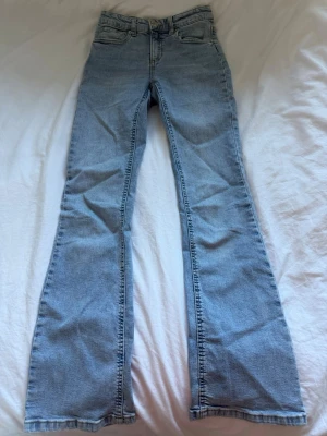 Ljusblå bootcut jeans - Säljer ett par ljusblå bootcut jeans med klassisk femficksdesign och hög midja. Jeansen har utsvängda ben och är gjorda i mjuk denim. Perfekta för dig som gillar retrovibbar och vill ha ett par bekväma jeans med snygg passform.