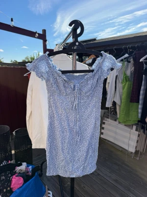 Blå blommig kortklänning med snörning - Söt blå kortklänning med små vita blommor och snörning framtill. Klänningen har volangdetaljer vid axlarna och är i storlek S💙