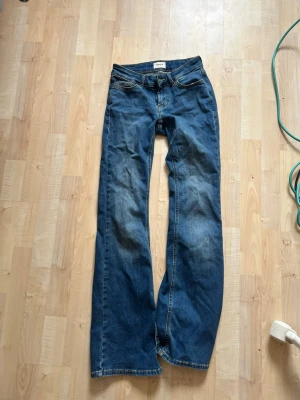 Blå bootcut jeans med slitningar - Säljer ett par blå bootcut jeans, Jeansen har klassisk femficksdesign och låg midja. Materialet är denim i bomull och passformen är avslappnad med utsvängda ben. Perfekta för en trendig och avslappnad stil.