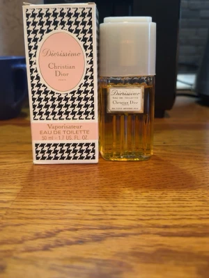 Diorissimo Eau de Toilette 50ml - Diorissimo Eau de Toilette från Christian Dior i 50 ml flaska. Flaskan är genomskinlig med guldfärgad vätska och vit kork. Förpackningen har ett klassiskt svartvitt mönster och rosa detaljer. En ikonisk doft som utstrålar elegans och lyx.