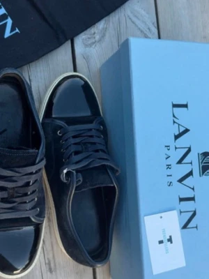 Lanvin  - Snygga svarta sneakers från Lanvin med vit sula och svarta skosnören. Skorna har en stilren design med ovandel i mocka och detaljer i blankt läder på tån. Perfekta för dig som gillar klassisk men modern stil.