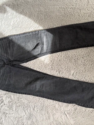 Grå raka jeans med slitning från Levi’s  - Snygga grå jeans från Levi’s med rak passform och klassiska fem fickor. Jeansen har en diskret slitning på ena benet och är tillverkade i ett mjukt denimtyg. Passar perfekt till en avslappnad streetstil.