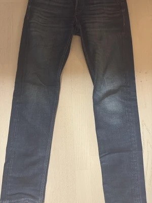 Mörkblå tapered jeans - Säljer ett par mörkblå jeans med tapered passform, modellen heter Mike. Jeansen har snygga slitningar och klassisk femficksdesign. Perfekta för dig som gillar en smalare siluett och vill ha ett par stilrena jeans till garderoben. Pris kan diskuteras!