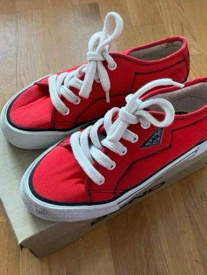 Röda vintage Vagabond canvas sneakers strl. 39 - Coola röda canvas-sneakers från Vagabond stl 39! ❤️ Modellen har tjockare sula och snygg retro-logga på sidan. Helt oanvända med krispigt ren undersula, endast legat förvarade i originalkartong. Finns ett mindre förvaringsspår på gummikanten där det svarta strecket nötts bort lite (se bild), men de är i ett fantastiskt fint skick! Levereras i kartong.