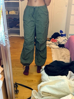 Gröna cargobyxor med dragsko - Säljer ett par gröna cargobyxor med avslappnad passform och dragsko i midjan. Byxorna har stora fickor på sidorna och resår vid bensluten för en cool och bekväm look. Perfekta för dig som gillar streetwear och vill ha något både snyggt och praktiskt. De är XXS fast passar bra även i S/M