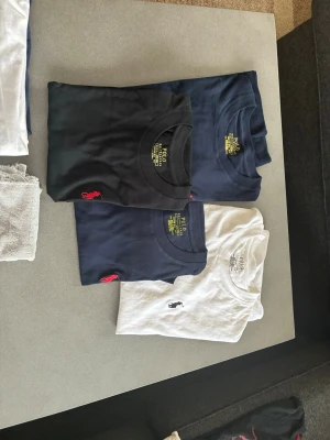 T-shirt pack från Polo Ralph Lauren - Säljer ett paket med fyra klassiska t-shirts från Polo Ralph Lauren. Två marinblå, en svart och en vit, alla med den ikoniska broderade loggan på bröstet. T-shirtsen är kortärmade och har en normal passform. Perfekta basplagg till garderoben.