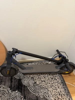 Hopfällbar elscooter med laddare - Säljer en svart hopfällbar elscooter med laddare. Scootern har en robust ram i metall, gummihjul och blå detaljer på handtagen. Perfekt för smidig transport i stan och enkel att ta med tack vare den vikbara designen. Hastighet: 25km/h Räckvidd: 30km