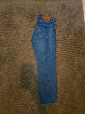 Levis jeans - Säljer ett par klassiska blå jeans med rak passform och en tydlig bakficka. Jeansen har en läderpatch i midjan och är i ett tidlöst denimtyg. Perfekta för dig som gillar enkel och stilren look.