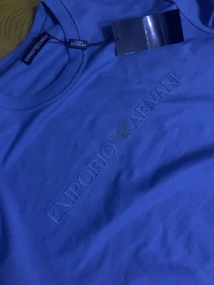 Blå sweatshirt från Emporio Armani - Snygg blå sweatshirt från Emporio Armani med diskret logga och emblem broderat på bröstet. Tröjan har rund halsringning, långa ärmar och ribbade muddar. Perfekt för en stilren och avslappnad look.