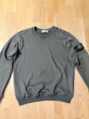 Olivgrön sweatshirt från Stone Island - Snygg olivgrön sweatshirt från Stone Island med klassisk rund halsringning och ribbade muddar. Tröjan har den ikoniska Stone Island-loggan på vänster ärm. Perfekt för en avslappnad och trendig stil. Passformen är perfekt 