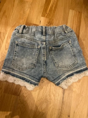 Barnshorts med spets - Barnshorts med vit spets i storlek 116 från Lindex. Har en liten fläck, därav priset men annars i mycket bra skick!