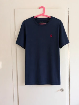 Polo Ralph Lauren T-shirt – mörkblå - Klassisk T-shirt från Polo Ralph Lauren i mörkblå/navy med den ikoniska broderade hästloggan i rött på bröstet. Färg: Mörkblå / Navy Märke: Polo Ralph Lauren Skick: Fint begagnat skick utan skador! Stilren och tidlös modell som är enkel att matcha med både jeans och shorts. ❤️💙 Skriv gärna vid frågor eller om du vill ha mått!