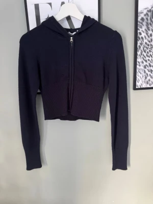 Mörkblå cropped  stickad hoodie med dragkedja - Snygg mörkblå  stickad hoodie med dragkedja framtill och huva. Modellen är cropped och har ribbstickad nederkant samt långa ärmar. Tillverkad i mjukt stickat material som ger en avslappnad vibe. Perfekt till jeans eller kjol för en trendig look.