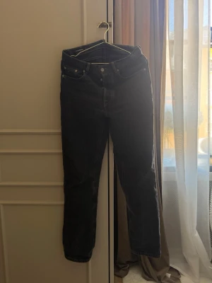 J.Lindeberg Svarta raka jeans med hög midja - Säljer ett par svarta jeans med rak passform och hög midja. Jeansen har klassiska fem fickor, knappgylf och är tillverkade i ett kraftigt denimtyg. Perfekta för en avslappnad och stilren look.