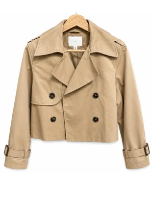 Kort beige trenchcoat med bälte - Snygg kort trenchcoat i beige med dubbelknäppning och passat XS-M. Jackan har bälte med spänne vid ärmsluten och stora knappar framtill. Perfekt för dig som vill ha en trendig och stilren look. Materialet ser ut att vara bomull eller en bomullsblandning.