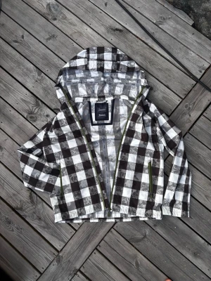 Unik Herno Windbreaker - Snygg vindjacka med mörkbrunt o vitt rutmönster och diskreta blommiga detaljer. Jackan har en stur huva som är anpassad för ute miljöer i både våt och torrt. Hel dragkedja framtill och två sidofickor med gröna dragkedjor. Perfekt för blåsiga dagar och enkel att matcha med jeans. Storlek 50 men passar även 48. Gåt att spänna åt på många ställen för att få den att passa perfekt. Inga defekter alls, som ny. Byte kan vara intressant!         Orginal Pris ligger runt 11000kr