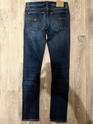 Nudie Jeans Tight Long John Mörkblå W29/L34 - Skinny Fit - Nudie Jeans Tight Long John ”Dark Superblue” mörkblå jeans med skinny fit-passform och låg midja, storlek W29/L34, midja 39 cm, ytterbenslängd 106,5 cm, benöppning 15 cm, modellen är 185cm & väger 65kg, i fint skick. 