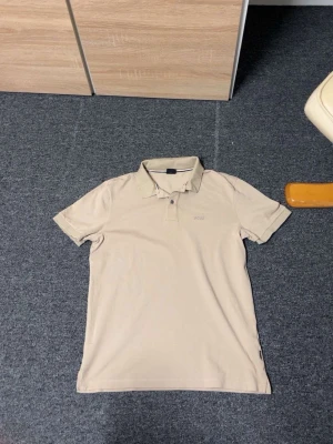 Beige pikétröja med krage - Snygg beige pikétröja med klassisk krage och korta ärmar. Tröjan har knappar vid halsen och en stilren look utan mönster. Perfekt till jeans eller shorts för en clean och enkel stil.
