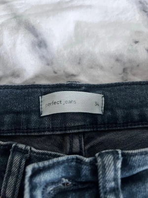 Mörkblå bootcut jeans perfect jeans - Säljer ett par mörkblå bootcut jeans från perfect jeans (gina tricot) i storlek 34. Jeansen har klassisk femficksmodell och utsvängda ben. Materialet är mjukt denim med stretch för extra komfort. Perfekta för dig som gillar retrovibbar och en snygg siluett.