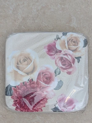 Snygg förvaring med blommönster för bindor och trosskydd  - Snygg förvaring för bindor och trosskydd med romantiskt blommönster i rosa, beige och rött. Asken har en fyrkantig form och är dekorerad med stora rosor och andra blommor på . Material troligen plåt eller metall . Helt oöppnad plast förpackning. Helt oanvänd ask