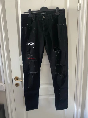 Svarta skinny jeans med slitningar - Säljer ett par svarta skinny jeans med slitningar och patchdetaljer.